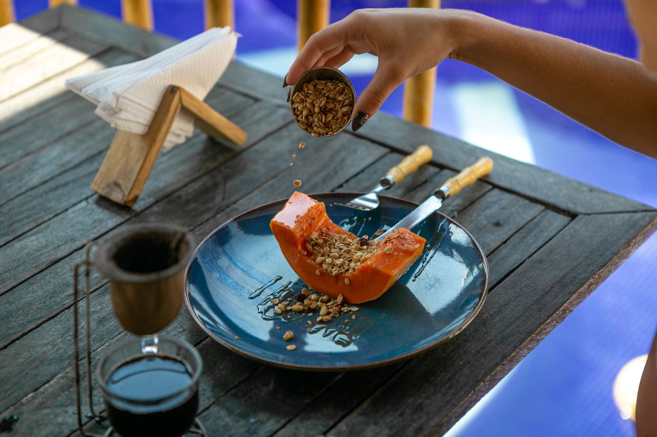 Prato azul com mamão e granola sendo servido